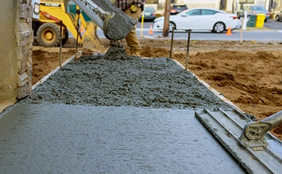 KSW Concrete is being poured and leveled on a construction site, with a worker and machinery visible in the background. Denver Metro